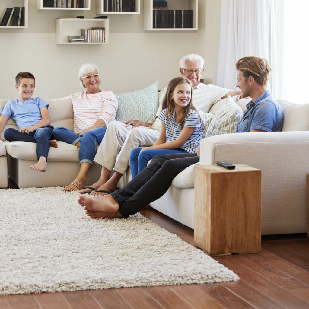 Happy family sitting on living room | Shans Carpets And Fine Flooring Inc